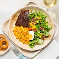 Biodegradable ChicLeaf Palm Leaf Plates with macaroni and cheese, steak, and salad on a light background