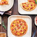 Wooden table with pizzas on biodegradable ChicLeaf Palm Leaf Party Plates, garnished with herbs.