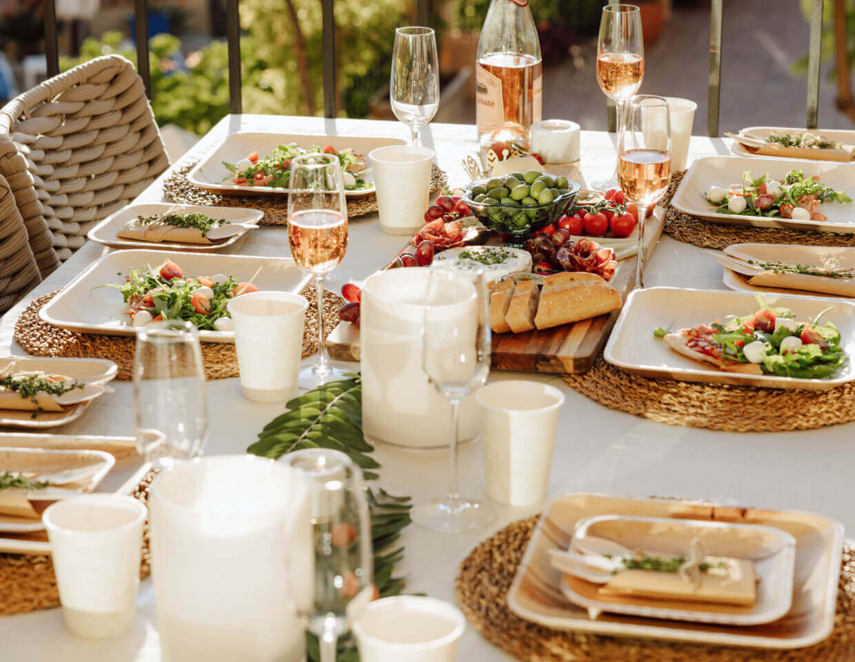Outdoor dining table set with biodegradable ChicLeaf Palm Leaf Plates, glasses, and food in a garden setting