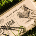 Hatortempt's reusable egg cartons with a rooster illustration and text 'Raised with Love, Laid in USA' on grass.