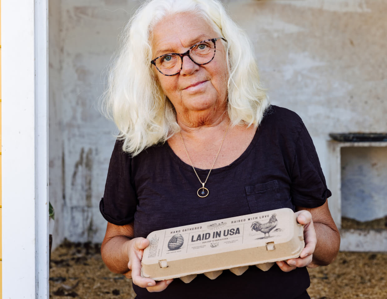 Woman holding Hatortempt's reusable, compostable carton of eggs labeled 'Laid in USA' in front of a rustic background.