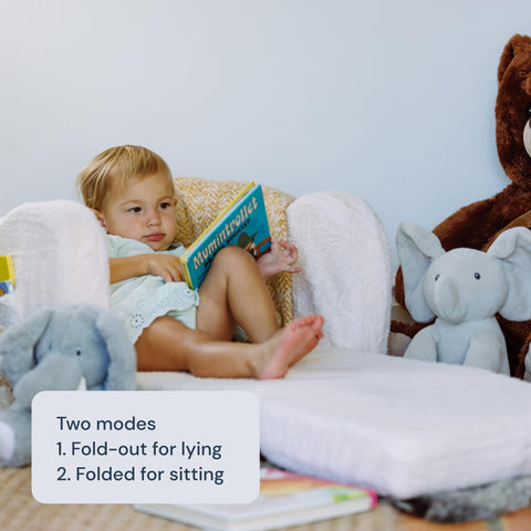 Child reading a book in Todale's transforming lounge chair and bed, with stuffed animals around