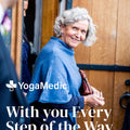 Woman in blue sweater standing in front of a wooden door with YogaMedic logo and text.