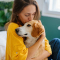 Woman in a yellow shirt hugging a dog indoors